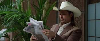 Movie still from “The Counselor” (2013), directed by Ridley Scott – A man wearing a cowboy hat reading a newspaper; Medium shot, Low angle