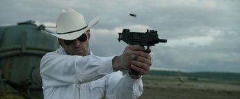 Movie still from “The Counselor” (2013), directed by Ridley Scott – A man wearing a white shirt and a white cowboy hat is holding a gun; Medium shot, Low angle
