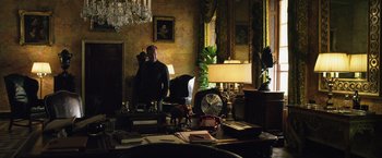 Movie still from “The Counselor” (2013), directed by Ridley Scott – A man sitting at a desk in front of a lamp; Wide shot, Over the shoulder angle