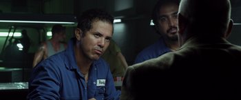 Movie still from “The Counselor” (2013), directed by Ridley Scott – A man sitting next to another man in a dark room; Medium shot, Over the shoulder angle