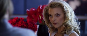 Movie still from “The Counselor” (2013), directed by Ridley Scott – A beautiful woman with blonde hair standing in front of a vase of red flowers; Close Up shot, Over the shoulder angle