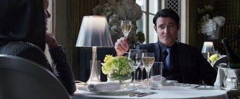 Movie still from “The Counselor” (2013), directed by Ridley Scott – A man sitting at a table with a glass of wine; Medium shot, Over the shoulder angle