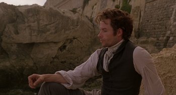 Movie still from “The Count of Monte Cristo” (2002), directed by Kevin Reynolds – A man sitting on the ground near some rocks; Medium shot, Low angle