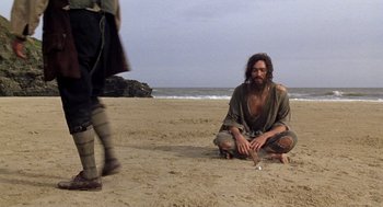 Movie still from “The Count of Monte Cristo” (2002), directed by Kevin Reynolds – A man sitting on the beach with a cigarette in his mouth; Wide shot, High angle