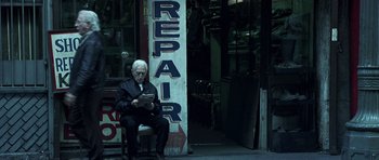 Movie still from “Phone Booth” (2002), directed by Joel Schumacher – An older man sitting in front of a repair shop; Wide shot, Low angle