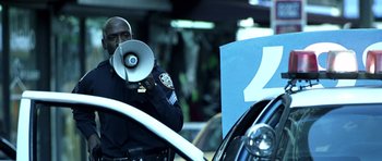 Movie still from “Phone Booth” (2002), directed by Joel Schumacher – A police officer holding a megaphone in front of a cop car; Medium shot, Low angle