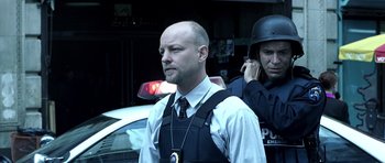 Movie still from “Phone Booth” (2002), directed by Joel Schumacher – A man in a police uniform standing in front of a cop car; Medium shot, Low angle