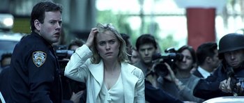 Movie still from “Phone Booth” (2002), directed by Joel Schumacher – A woman in a white jacket standing in front of a camera; Close Up shot, Over the shoulder angle