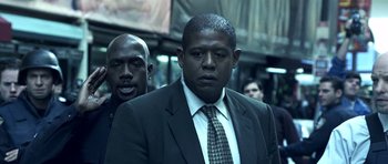 Movie still from “Phone Booth” (2002), directed by Joel Schumacher – A man in a suit and tie standing next to another man in a suit and tie; Close Up shot, Over the shoulder angle