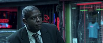 Movie still from “Phone Booth” (2002), directed by Joel Schumacher – A man in a suit and tie sitting in front of neon signs; Close Up shot, Low angle