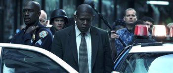 Movie still from “Phone Booth” (2002), directed by Joel Schumacher – A man in a suit and tie standing next to a police car; Medium shot, Over the shoulder angle