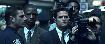 Movie still from “Phone Booth” (2002), directed by Joel Schumacher – A man in a suit and tie standing in front of a camera; Close Up shot, Over the shoulder angle