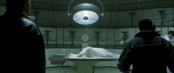Movie still from “The Crimson Rivers” (2000), directed by Mathieu Kassovitz – An autopsy table in an industrial setting with a light hanging from the ceiling; Wide shot, High angle