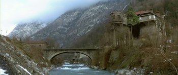 Movie still from “The Crimson Rivers” (2000), directed by Mathieu Kassovitz – A bridge over a river near a mountain; Extreme Wide shot, High angle