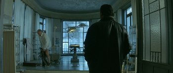 Movie still from “The Crimson Rivers” (2000), directed by Mathieu Kassovitz – A man standing in front of a window in a room; Wide shot, Low angle