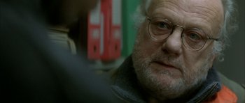 Movie still from “The Crimson Rivers” (2000), directed by Mathieu Kassovitz – An older man wearing glasses looking at the camera; Close Up shot, Over the shoulder angle