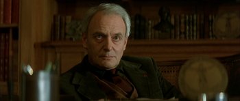 Movie still from “The Crimson Rivers” (2000), directed by Mathieu Kassovitz – An older man sitting in a chair in a room; Close Up shot, Low angle