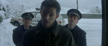 Movie still from “The Crimson Rivers” (2000), directed by Mathieu Kassovitz – A man standing next to two police officers; Medium shot, Low angle