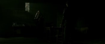 Movie still from “The Crimson Rivers” (2000), directed by Mathieu Kassovitz – Two people in a dark room , one of whom is sitting at a table; Wide shot, Over the shoulder angle