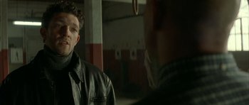 Movie still from “The Crimson Rivers” (2000), directed by Mathieu Kassovitz – A man in a black leather jacket standing next to another man; Close Up shot, Over the shoulder angle