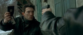 Movie still from “The Crimson Rivers” (2000), directed by Mathieu Kassovitz – A man holding a gun up to the side of a building; Close Up shot, Over the shoulder angle