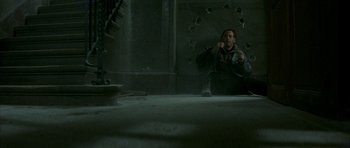 Movie still from “The Crimson Rivers” (2000), directed by Mathieu Kassovitz – A man sitting on the ground in front of a hole in the wall; Wide shot, Overhead angle