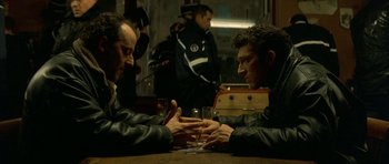 Movie still from “The Crimson Rivers” (2000), directed by Mathieu Kassovitz – Two men sitting at a wooden table with a glass of wine; Medium shot, High angle