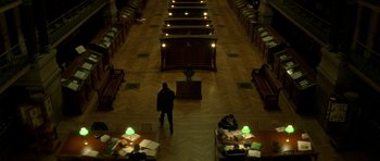 Movie still from “The Crimson Rivers” (2000), directed by Mathieu Kassovitz – A man standing in a room next to a desk; Extreme Wide shot, High angle