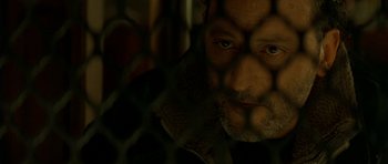 Movie still from “The Crimson Rivers” (2000), directed by Mathieu Kassovitz – A person behind a chain link fence; Close Up shot, High angle