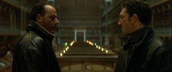 Movie still from “The Crimson Rivers” (2000), directed by Mathieu Kassovitz – Two men are standing in a library looking at each other; Close Up shot, Low angle