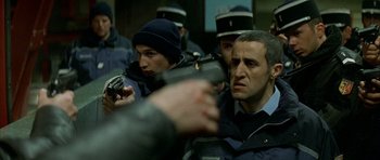 Movie still from “The Crimson Rivers” (2000), directed by Mathieu Kassovitz – A group of men standing next to each other holding guns; Medium shot, Over the shoulder angle