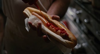 Movie still from “The Crow” (1994), directed by Alex Proyas – A person holding a hot dog in a bun with ketchup; Extreme Close Up shot, Overhead angle