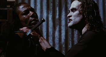 Movie still from “The Crow” (1994), directed by Alex Proyas – A man is holding a knife in his hand while a woman is holding a knife in her hand; Close Up shot, Over the shoulder angle