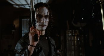 Movie still from “The Crow” (1994), directed by Alex Proyas – A person holding a gun in a room; Close Up shot, Low angle