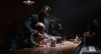 Movie still from “The Crow” (1994), directed by Alex Proyas – Two men sitting at a table and one man is holding a knife; Medium shot, Low angle