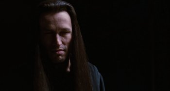 Movie still from “The Crow” (1994), directed by Alex Proyas – A man with long black hair and a black shirt; Close Up shot, Low angle