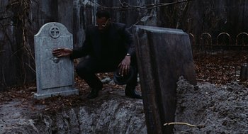 Movie still from “The Crow” (1994), directed by Alex Proyas – A man kneeling down next to an old grave; Medium shot, Low angle