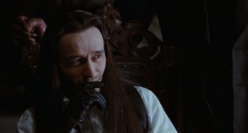 Movie still from “The Crow” (1994), directed by Alex Proyas – A man with long black hair is smoking a pipe; Close Up shot, Over the shoulder angle