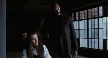 Movie still from “The Crow” (1994), directed by Alex Proyas – A man standing next to another man with long hair; Medium shot, Over the shoulder angle