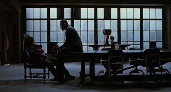 Movie still from “The Crow” (1994), directed by Alex Proyas – A man sitting at a table in front of a window; Wide shot, Over the shoulder angle