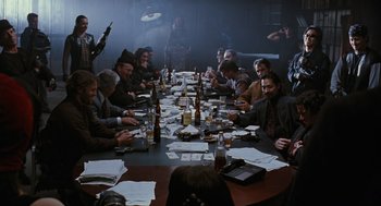 Movie still from “The Crow” (1994), directed by Alex Proyas – A group of people sitting at a table with papers on it; Wide shot, High angle