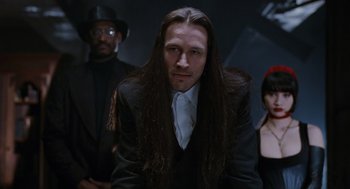 Movie still from “The Crow” (1994), directed by Alex Proyas – A man with long black hair standing next to two other people; Close Up shot, Low angle