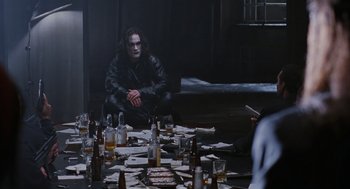 Movie still from “The Crow” (1994), directed by Alex Proyas – A man sitting in front of a bunch of bottles; Medium shot, Over the shoulder angle
