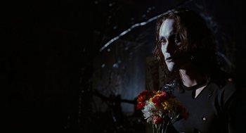 Movie still from “The Crow” (1994), directed by Alex Proyas – A man with a white face holding a bouquet of flowers; Medium shot, Low angle