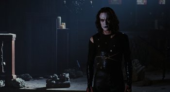 Movie still from “The Crow” (1994), directed by Alex Proyas – A man in a black outfit standing in a dark room; Medium shot, Low angle