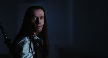 Movie still from “The Crow” (1994), directed by Alex Proyas – A man with long black hair wearing a white shirt; Close Up shot, Low angle