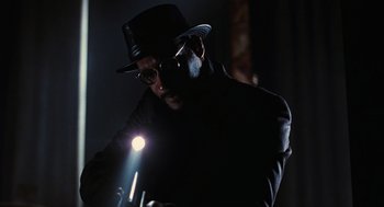 Movie still from “The Crow” (1994), directed by Alex Proyas – A man wearing a hat and glasses is holding a flashlight; Close Up shot, Low angle