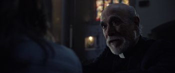 Movie still from “The Curse of La Llorona” (2019), directed by Michael Chaves – An old man with a beard is sitting in front of a stained glass window; Close Up shot, Over the shoulder angle
