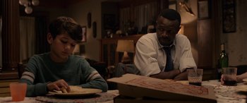 Movie still from “The Curse of La Llorona” (2019), directed by Michael Chaves – Two people sitting at a table with a box of pizza in front of them; Medium shot, Over the shoulder angle