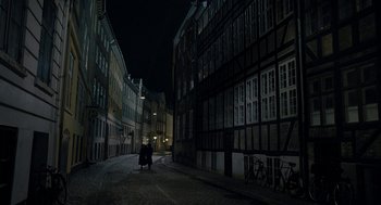 Movie still from “The Danish Girl” (2015), directed by Tom Hooper – A person riding a bike down a street at night; Extreme Wide shot, High angle